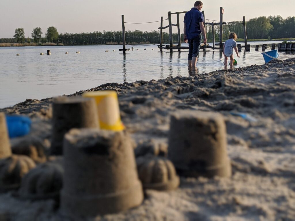 sandcastle by a lake, father and son in the background